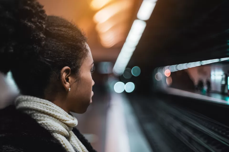 Close-up of woman waiting on fairly empty subway platform with tracks and opposing platform blurred in the background.
